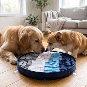 Könnte beinhalten: Ein runder, marineblauer Hunde-Puzzle-Matte mit einem farbblockierten Design in Grau-, Weiß- und Blautönen. Zwei Hunde, ein Golden Retriever und ein Corgi, interagieren mit der Matte auf einem Holzboden.