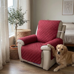 Könnte beinhalten: Eine bordeauxfarbene, gesteppte Relaxsessel-Abdeckung bedeckt einen cremefarbenen Relaxsessel. Die Abdeckung schützt Rücken, Sitzfläche und Armlehnen des Stuhls. Ein Golden Retriever liegt auf dem Boden neben dem Stuhl. Ein Olivenbaum im Topf und ein Weidenkorb sind im Hintergrund.