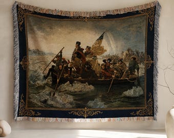 May include: Woven tapestry throw blanket featuring the iconic painting "Washington Crossing the Delaware." The artwork depicts a historical scene with figures in a boat, set against a backdrop of water and sky. The blanket has a navy blue border with decorative gold accents and fringe.