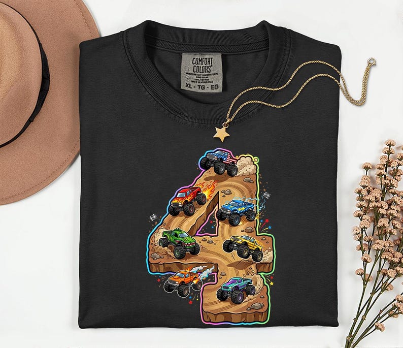 May include: Black crew neck sweatshirt featuring a colourful graphic of monster trucks racing on a number 4. The graphic includes red, green, blue, and yellow trucks. A gold necklace with a star pendant is on the shirt.