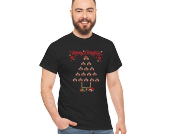 May include: A black t-shirt featuring a graphic of a Christmas tree constructed from brown footballs. The text Merry Christmas is printed in red above the tree, which sits atop a goalpost base with small gift boxes and a Santa hat.