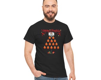 May include: A black t-shirt featuring a graphic of a Christmas tree constructed from orange basketballs. At the top is a basketball hoop, and the text Merry Christmas is written in red script. Small gifts and a Santa hat are at the base.