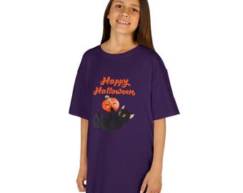 May include: A dark purple t-shirt featuring a graphic of a black cat lying on its back and holding a small orange pumpkin. Above the cat, the text Happy Halloween is printed in an orange, rounded, cursive font. The shirt has short sleeves.