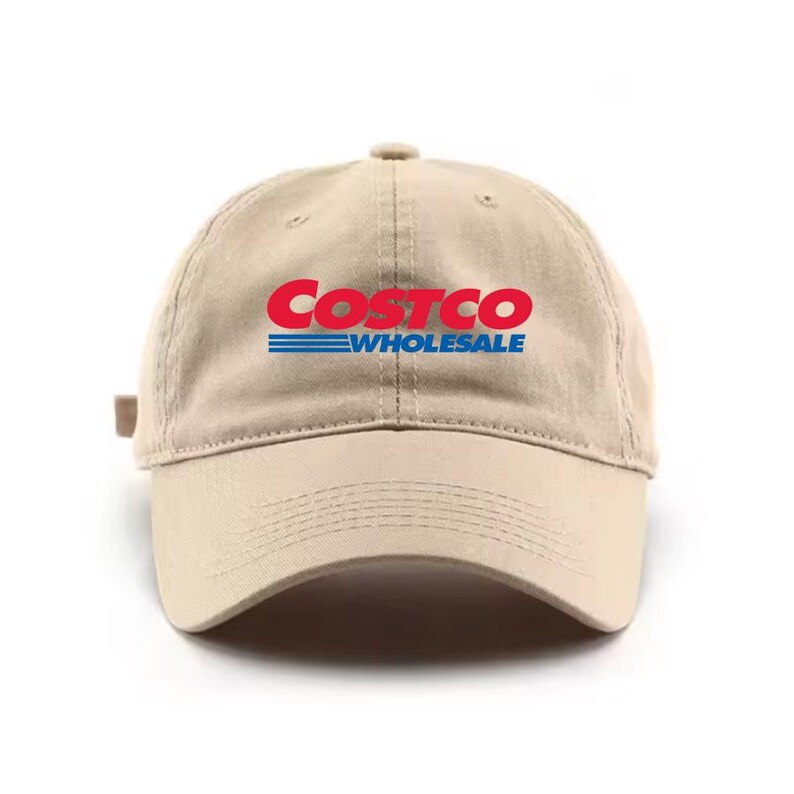 May include: A tan baseball cap with the Costco Wholesale logo in red and blue. The hat has a curved brim and an adjustable strap at the back. The logo is centered on the front of the cap.