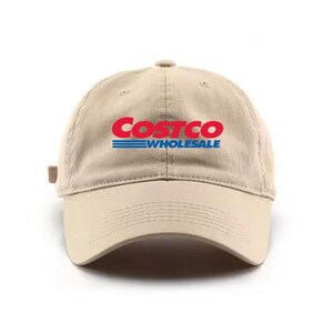 May include: A tan baseball cap with the Costco Wholesale logo in red and blue. The hat has a curved brim and an adjustable strap at the back. The logo is centered on the front of the cap.