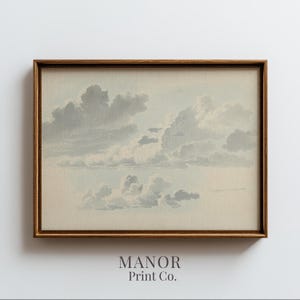 May include: A framed print of a cloudy sky in shades of gray and blue. The artwork features a detailed depiction of cumulus clouds. The frame is a warm brown color. The text "MANOR Print Co." is at the bottom.