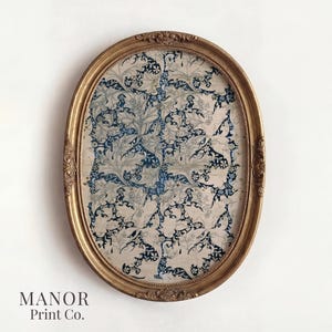 May include: An oval-shaped framed print with a gold-colored ornate frame. The print features a blue and off-white floral pattern. The text "MANOR Print Co." is printed at the bottom of the frame.
