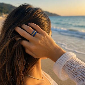 May include: A ring featuring a wide band with two vibrant blue outer edges and a central gold-toned stripe. The ring has a smooth, polished finish and a uniform width, displaying a distinct tri-color layered design across its circular surface.
