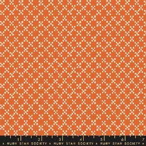 May include: Orange fabric featuring a repeating pattern of small, off-white, four-petal flower shapes. The fabric has a textured appearance. A ruler at the bottom shows the text "RUBY STAR SOCIETY".