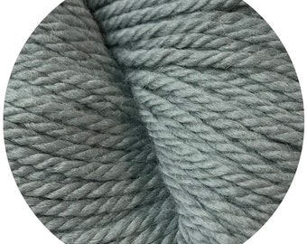 May include: Close-up of a skein of soft, gray yarn. The yarn is tightly wound and has a slightly textured surface.