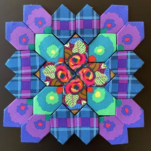 May include: A colorful patchwork quilt block with a floral design. The block features various geometric shapes in shades of blue, purple, green, and red. The central design showcases vibrant flowers, while the surrounding pieces display plaid and floral patterns.
