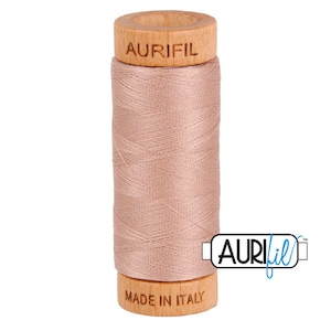 May include: A spool of light pink thread with a wooden bobbin. The bobbin is labeled "Aurifil" and "Made in Italy".