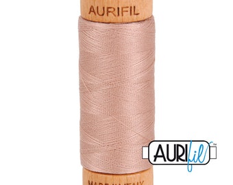 May include: A spool of light pink thread with a wooden bobbin. The bobbin is labeled "Aurifil" and "Made in Italy".
