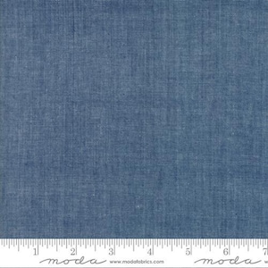 May include: Close-up of a blue fabric with a textured weave. The fabric has a denim-like appearance and is marked with a ruler along the bottom edge. The fabric is likely used for sewing, quilting, or other craft projects.