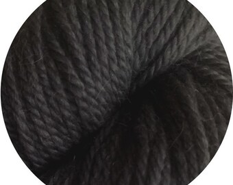 May include: A close-up of a ball of dark gray yarn. The yarn appears soft and textured, with visible strands and a slightly fuzzy appearance. The yarn is tightly wound, creating a dense, compact form.