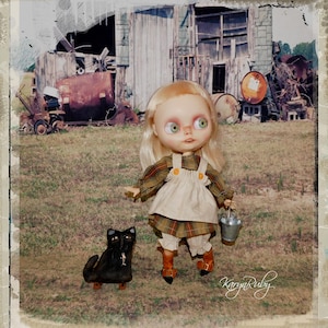 Könnte beinhalten: Eine Puppe im Vintage-Stil mit blonden Haaren und grünen Augen, die ein kariertes Oberteil, cremefarbene Latzhosen und braune Stiefel trägt. Eine schwarze Katzenfigur befindet sich in der Nähe. Die Puppe hält einen kleinen Metalleimer. Der Hintergrund zeigt eine rustikale Scheune und landwirtschaftliche Geräte.