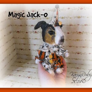 Peut inclure: Un chien en peluche noir et blanc portant un chapeau de jester et un costume sur le thème d'Halloween avec des couleurs orange, noir et blanc. Le chien tient une balle jaune et orange dans sa gueule. Le texte "Magic Jack-o" est écrit au-dessus du chien. Le texte "Karyn Ruby 2014" est écrit dans le coin inférieur droit de l'image.
