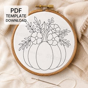 May include: A wooden embroidery hoop containing white fabric with a black line art pattern of a pumpkin topped with flowers and leaves. The text PDF TEMPLATE DOWNLOAD is visible in the upper left corner. A sewing needle rests below the hoop.