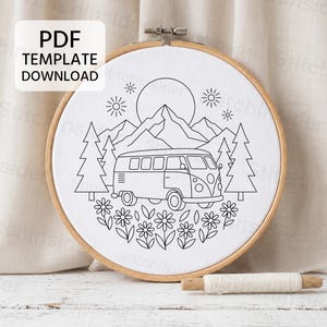 May include: A circular wooden embroidery hoop containing white fabric with a black line art pattern of a camper van, mountains, pine trees, flowers, and a sun. The text PDF TEMPLATE DOWNLOAD is visible in the upper left corner of the image.