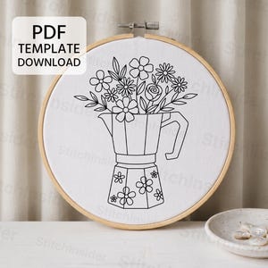 May include: A circular wooden embroidery hoop containing white fabric with a black line art pattern of a moka pot filled with various flowers. The base of the moka pot is decorated with small flower motifs. A box labeled PDF TEMPLATE DOWNLOAD is visible.