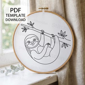 Puede incluir: Un bastidor de bordado circular de madera que contiene tela blanca con una ilustración de líneas negras de un perezoso colgado de una rama. El texto PDF TEMPLATE DOWNLOAD es visible en la esquina superior izquierda de la imagen.