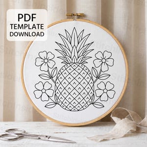 Puede incluir: Un bastidor de bordado circular de madera que contiene tela blanca con un diseño de líneas negras de una piña centrada entre cuatro flores. El texto PDF TEMPLATE DOWNLOAD está impreso en la esquina superior izquierda de la imagen.