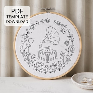 May include: A circular wooden embroidery hoop containing white fabric with a black line art pattern of a vintage gramophone centered within a floral wreath. A white rectangular box with the text PDF TEMPLATE DOWNLOAD is visible.