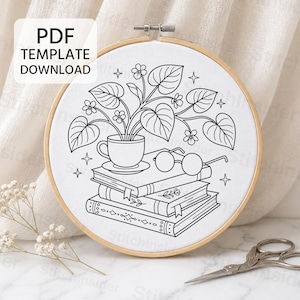 May include: A circular wooden embroidery hoop containing white fabric with a black line art design of a potted plant in a teacup resting on a stack of three books with a pair of round glasses. The text PDF TEMPLATE DOWNLOAD is visible.