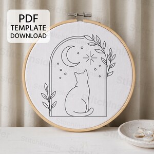 Könnte beinhalten: Ein runder Holzstickrahmen mit weißem Stoff, der ein schwarzes Linienkunst-Design einer Katze in einem Torbogen zeigt. Das Motiv umfasst eine Mondsichel, einen Stern und Blattzweige. Ein Etikett trägt die Aufschrift PDF TEMPLATE DOWNLOAD.