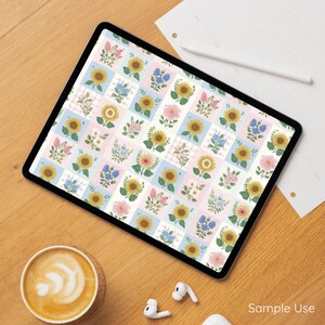 Op de afbeelding: Een digitale tablet toont een bloemenpatroon met zonnebloemen, roze rozen en blauwe bloemen op een witte en pastelkleurige achtergrond. De tablet ligt op een houten oppervlak met een kopje koffie, oortelefoons en een potlood.