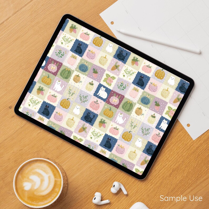 May include: A digital tablet screen displaying a repeating pattern of square tiles featuring illustrations of black and white cats, various pumpkins in shades of orange, pink, and green, and small sprigs of green foliage on a light background.