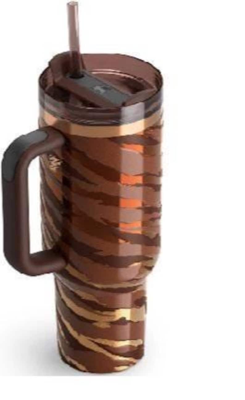K&ouml;nnte beinhalten: Ein brauner und goldener isolierter Becher mit Griff und Strohhalm. Der Becher hat ein Tigerstreifenmuster und einen dunkelbraunen Deckel. Der Griff ist dunkelbraun mit einem schwarzen Akzent.