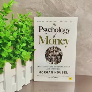 May include: A hardcover book titled "The Psychology of Money" with a brain illustration. The cover is white with gold lettering and the author's name, Morgan Housel. The book is a bestseller, with a quote from Jason Zweig.