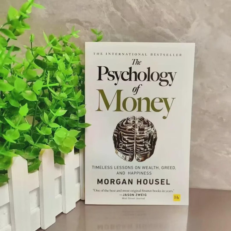 May include: A hardcover book titled "The Psychology of Money" with a brain illustration. The cover is white with gold lettering and the author's name, Morgan Housel. The book is a bestseller, with a quote from Jason Zweig.