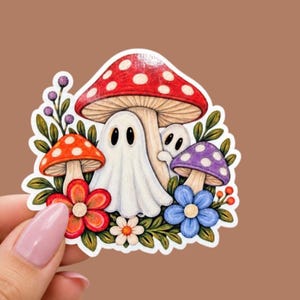 May include: A die-cut sticker featuring a large red mushroom with white spots, a smaller orange mushroom, and a purple mushroom. Two white ghosts with black eyes are nestled among the mushrooms, surrounded by red, blue, and white flowers.