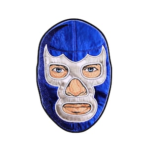 May include: A blue and silver embroidered patch shaped like a wrestling mask. The design features a vibrant blue fabric base with a silver mask overlay, showcasing detailed stitching for the eyes, nose, and mouth with realistic skin-toned thread.
