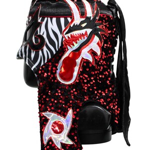 May include: A black and red lucha libre wrestling mask with a dragon design. The mask features a zebra print, red sequins, and a dragon head with sharp teeth. The mask has a black satin finish and long black ties.
