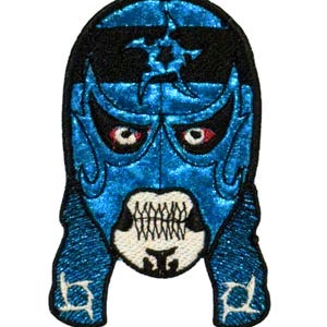 May include: A blue and black embroidered patch featuring a stylized mask design. The mask has a blue glitter finish with black accents, red eyes, and a white mouth with teeth. The patch is likely for clothing or accessories.