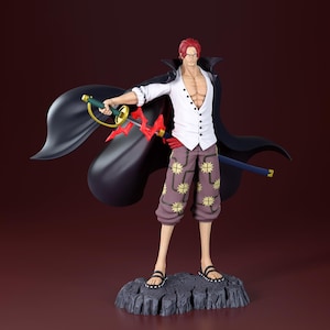May include: A detailed figurine of a character with red hair, wearing a white shirt, patterned pants, and a black cape. The figure holds a sword with a red and gold hilt and a blue sword. The figure stands on a gray rock base.