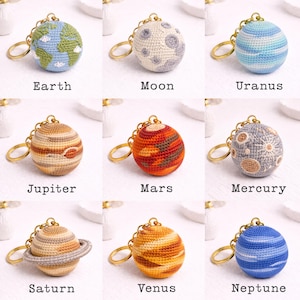 May include: Nine crocheted planet keychains, each with a gold-colored keyring. The planets include Earth, Moon, Uranus, Jupiter, Mars, Mercury, Saturn, Venus, and Neptune. Each planet is a different color and design, with the planet's name printed below.