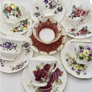 May include: A collection of vintage teacups and saucers. The cups and saucers feature floral designs in various colors, including red, purple, yellow, and white. Some have gold trim.