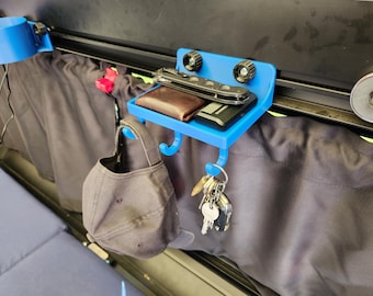 Könnte beinhalten: Ein blauer 3D-gedruckter Organizer mit einem Regal, Haken und einem Becherhalter. Das Regal enthält eine Brieftasche, ein Messer und einen Schlüsselanhänger. Eine Baseballkappe hängt an einem Haken, und Schlüssel hängen darunter. Der Organizer ist auf einer dunklen Oberfläche montiert.