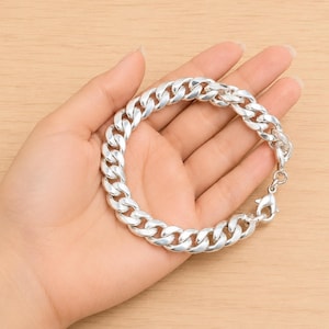 Op de afbeelding: Een gepolijste zilverkleurige gourmetarmband met dikke, in elkaar grijpende ovale schakels. De armband is voorzien van een stevige karabijnsluiting en heeft een hoogglanzende metalen afwerking die het licht reflecteert op het gladde oppervlak.