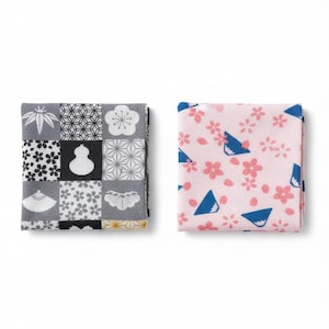 以下が含まれることがあります： 2つの折り畳まれた正方形の布。1つは、花柄と幾何学模様のグレー、黒、白のパッチワークデザインです。もう1つは、ピンクの花と青い三角形のパターンです。