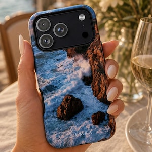 Może przedstawiać: Etui na smartfona z wysokiej rozdzielczości nadrukiem fotograficznym przedstawiającym surowe klify przybrzeżne i rozbijające się fale oceanu. Etui posiada czarny moduł aparatu oraz napis LUMRA małymi białymi literami przy dolnej krawędzi.