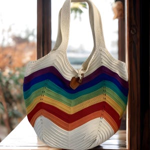 May include: A white and rainbow-striped tote bag with a woven design. The bag features a cream-colored handle and a brown leather tag. The bag's body is a vibrant display of rainbow colors, creating a cheerful and eye-catching accessory.