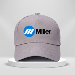 Puede incluir: Gorra de béisbol gris con el logotipo de Miller. El logotipo presenta un círculo azul con tres rayas blancas y el nombre de la marca en negro. La gorra se muestra sobre un pedestal blanco.