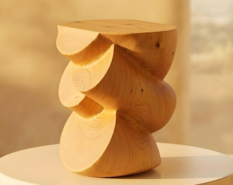 May include: A light-colored wooden stool featuring a sculptural, twisted, and undulating form with visible wood grain patterns. The object has a flat, circular top surface and a continuous, flowing silhouette that curves inward and outward.