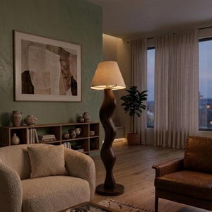 Puede incluir: Una lámpara de pie alta de madera oscura con un diseño ondulado y una pantalla beige. Se encuentra en un salón con una paleta de colores neutros, un sillón beige, una silla de cuero marrón y un mueble de madera. El ambiente es acogedor.