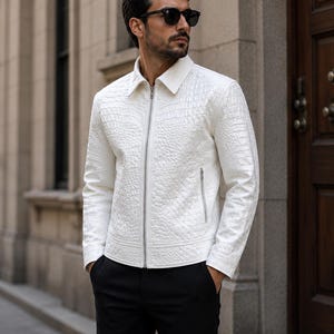 May include: A white zip-up jacket with a textured crocodile-skin pattern, featuring a classic collar, long sleeves, and two side pockets with silver zips, paired with solid black trousers and dark-tinted sunglasses.